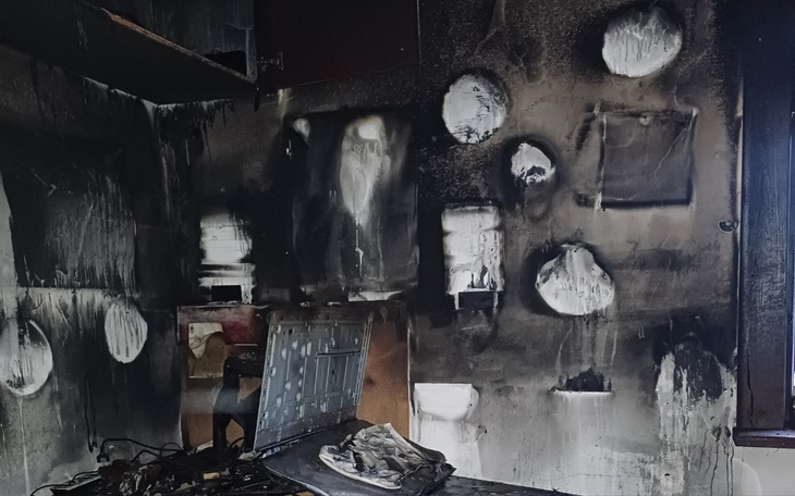 Zniszczony pokój po pożarze, czarne ściany i uszkodzone meble.