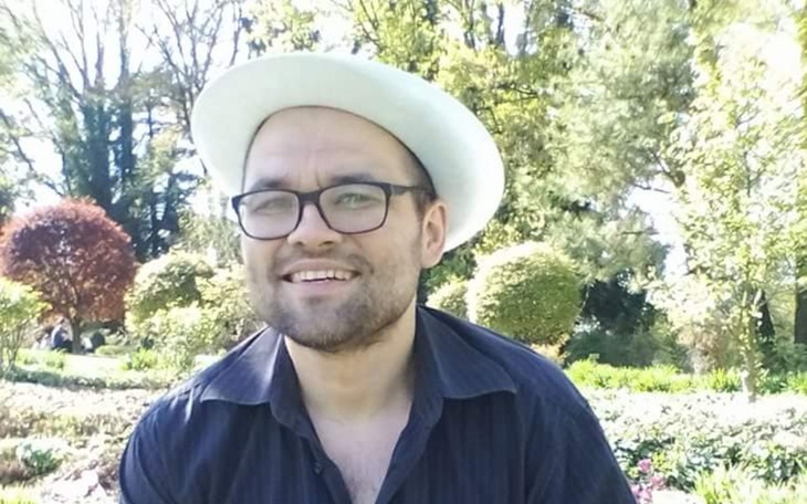 Mężczyzna w białym kapeluszu uśmiecha się w ogrodzie.