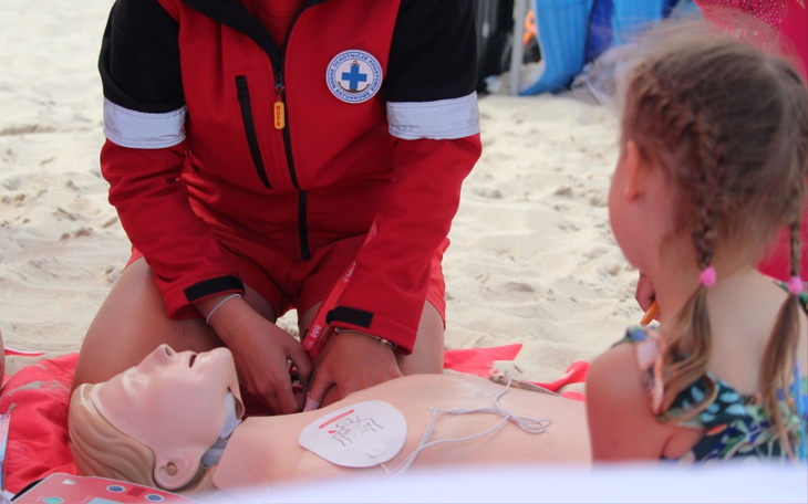 Ratownik medyczny uczy dziecko resuscytacji na plaży.