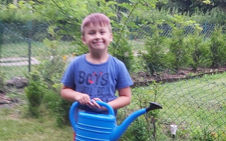 Chłopiec trzymający niebieską konewkę w ogrodzie.