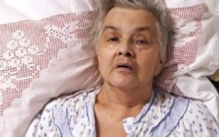 Starsza kobieta leżąca w łóżku, z wyrazem twarzy pełnym smutku.