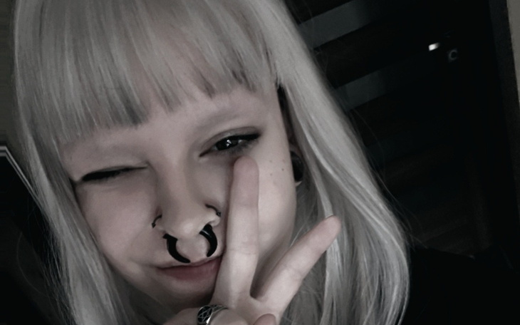 Młoda kobieta z białymi włosami robi znak pokoju w ciemnym otoczeniu.