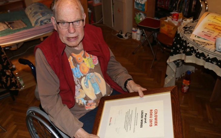 Starszy mężczyzna z dyplomem w ręku, uśmiechający się.