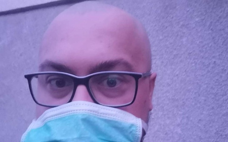 Mężczyzna w okularach i masce, selfie na tle szarej ściany.