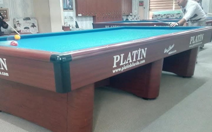 Stół bilardowy z niebieskim stołem, w tle grający mężczyzna.