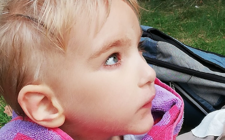 Małe dziecko z różowym kapturem, patrzy w górę.