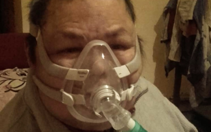 Osoba z maską tlenową, siedząca w pomieszczeniu.