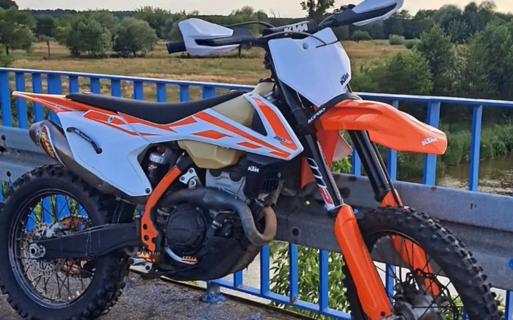 Motocykl terenowy na tle zieleni, gotowy do jazdy.