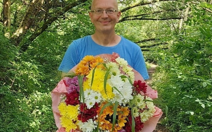 Mężczyzna trzymający bukiet kwiatów w zielonym otoczeniu.