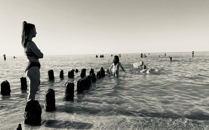 Kobieta na plaży, w tle ludzie kąpiący się w morzu.