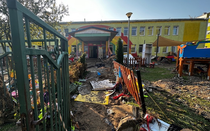 Zniszczony plac zabaw po powodzi, zniszczenia widoczne w tle.
