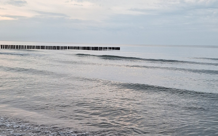 Spokojna plaża z falami, drewniane pomosty w oddali.