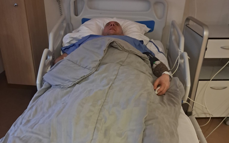 Mężczyzna leżący w szpitalnym łóżku, w niebieskim szpitalnym ubraniu.