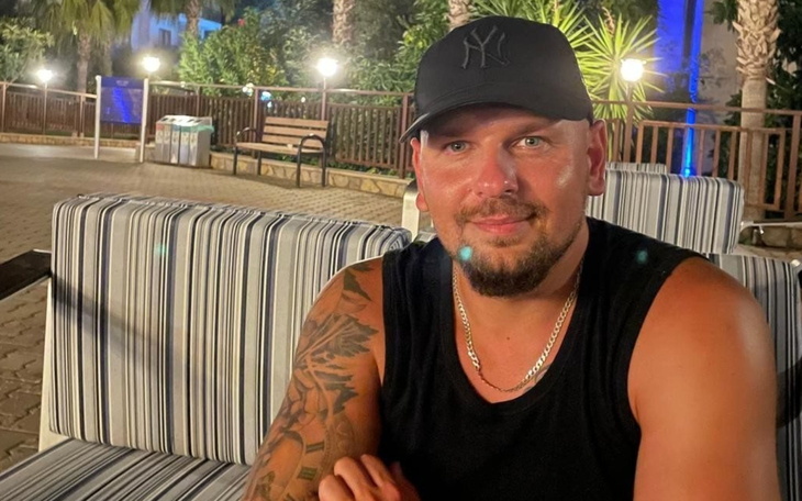 Mężczyzna w czapce, siedzący na kanapie w letnim otoczeniu.