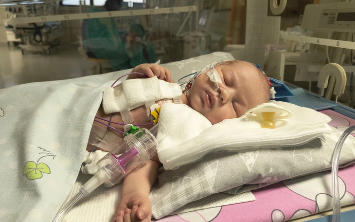 Noworodek w inkubatorze, otoczony sprzętem medycznym.