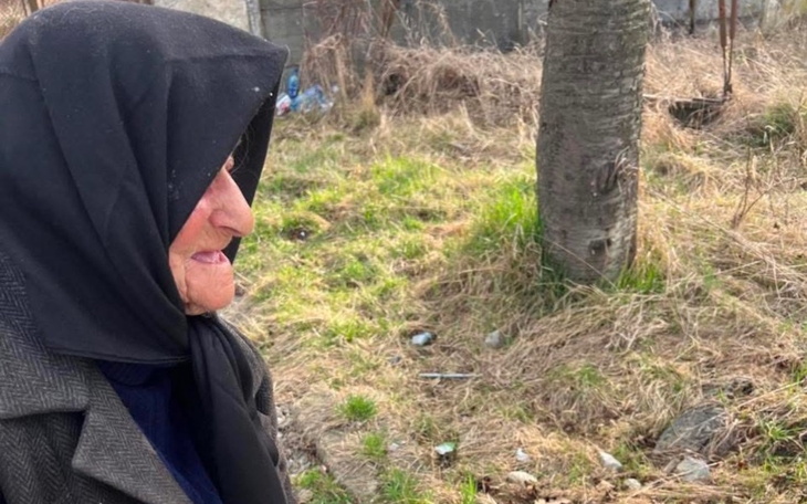 Starsza kobieta w tradycyjnym stroju na tle przyrody.