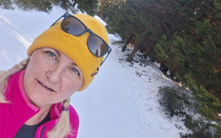 Kobieta w żółtej czapce na tle zaśnieżonego lasu.