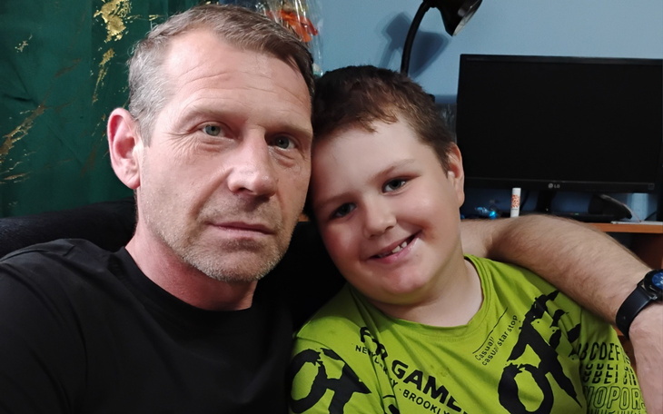 Mężczyzna z dzieckiem, obaj uśmiechnięci na kanapie.