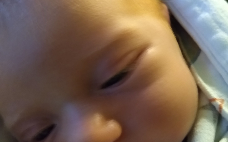 Zbliżenie na twarz noworodka, z delikatnym uśmiechem.