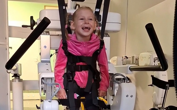 Uśmiechnięta dziewczynka w sprzęcie rehabilitacyjnym.