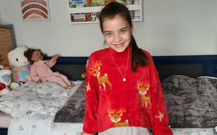 Dziewczynka w czerwonym swetrze z reniferami, uśmiechająca się do kamery.