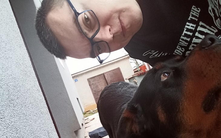 Mężczyzna z okularami selfie z psem w tle.