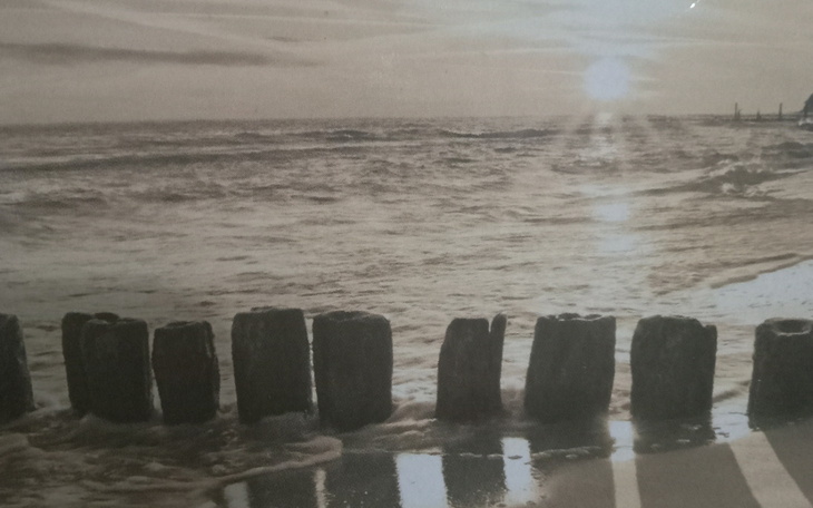 Stare zdjęcie plaży z drewnianymi palami, w tle zachód słońca.