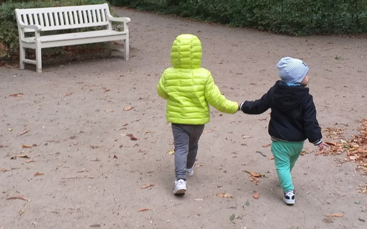 Dwoje dzieci trzyma się za ręce, spacerując po parku.