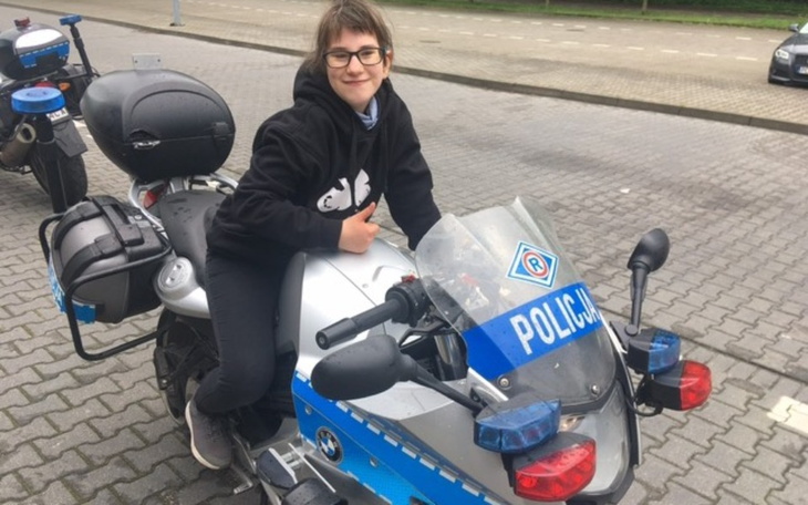 Młoda dziewczyna siedzi na motocyklu policyjnym, uśmiecha się.