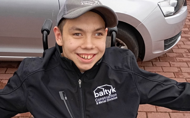 Młody chłopak uśmiechający się w wózku inwalidzkim.