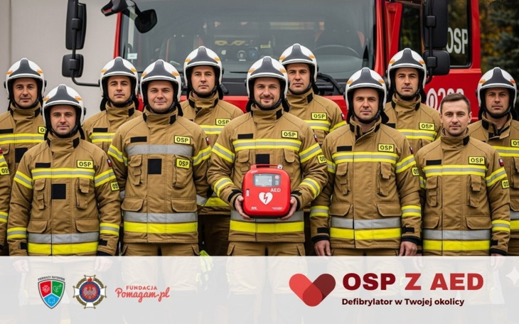 Grupa strażaków w mundurach, pozująca przed wozem strażackim.