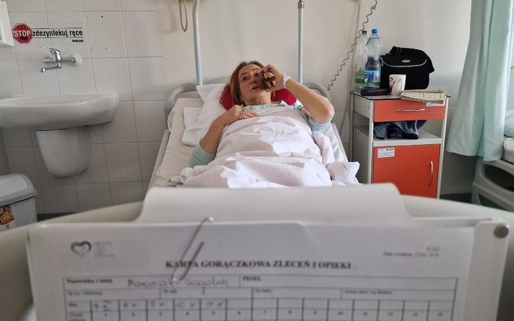 Kobieta leżąca w szpitalnym łóżku, rozmawiająca przez telefon.