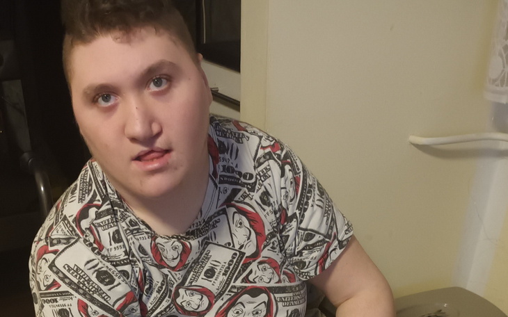 Młody mężczyzna w koszulce z motywem dolarów, patrzy w obiektyw.