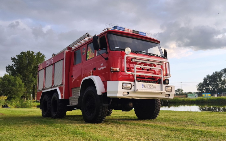 Czerwony wóz strażacki na tle zieleni.