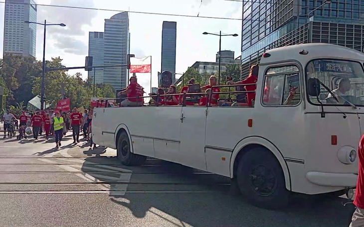 Biały autobus z ludźmi w czerwonych koszulkach na paradzie.