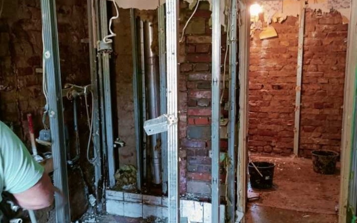 Zniszczona łazienka w trakcie remontu, widoczne cegły i rury.