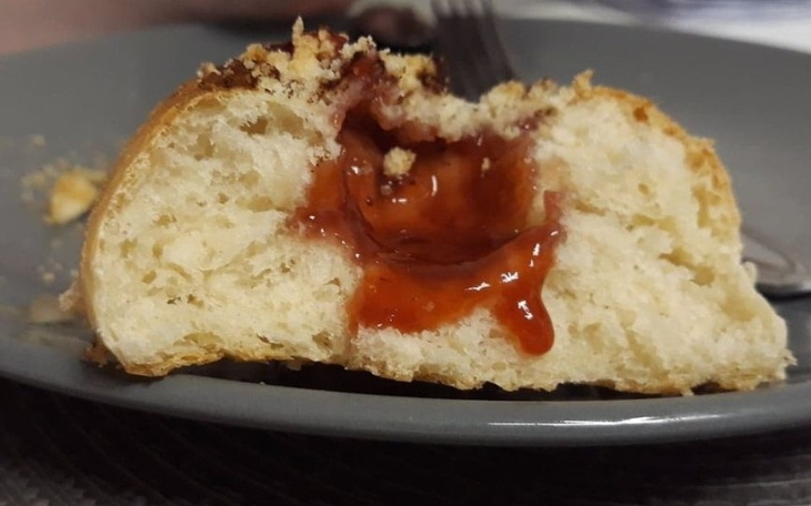 Przekrojony pączek z dżemem truskawkowym w środku.