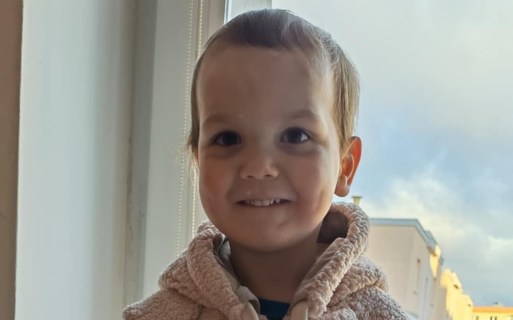 Uśmiechnięty chłopiec w ciepłej bluzie, stojący przy oknie.