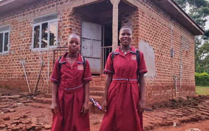 Dwie dziewczynki w mundurkach szkolnych przed budynkiem.