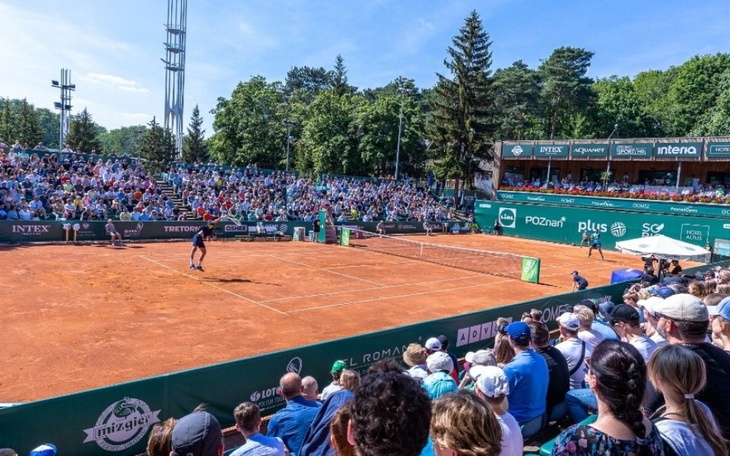 Mecz tenisa na korcie, widownia pełna kibiców.