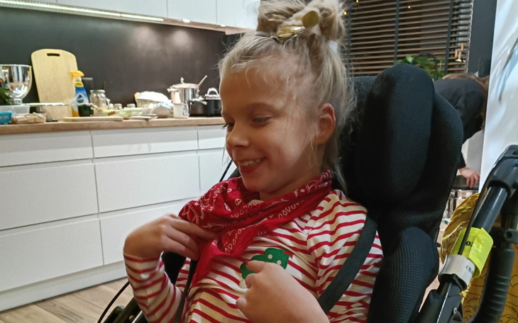 Uśmiechnięta dziewczynka w wózku, z chustą na szyi.