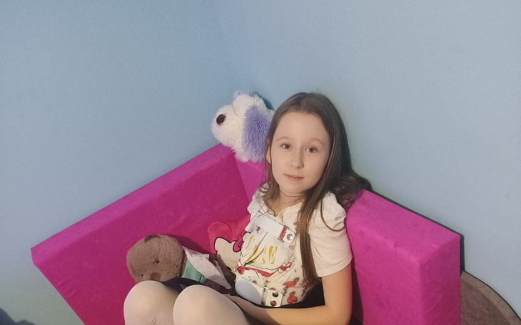 Dziewczynka siedząca na różowym fotelu z pluszakami.