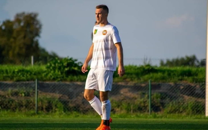 Młody piłkarz na boisku, w białym stroju.