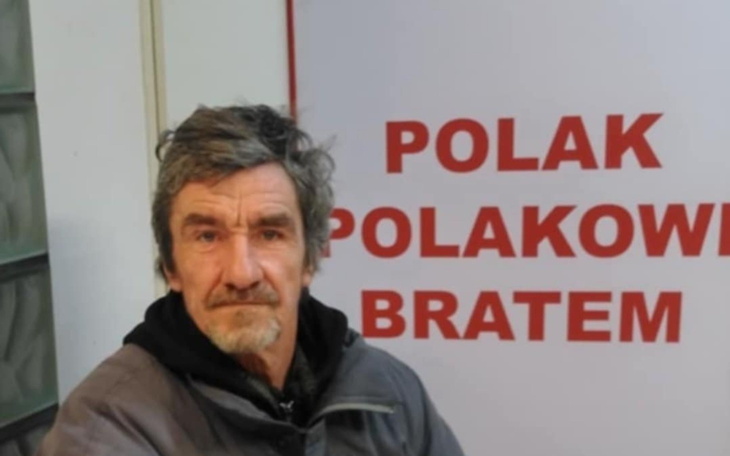 Mężczyzna siedzący przed napisem 'Polak Polakowi Bratem'.