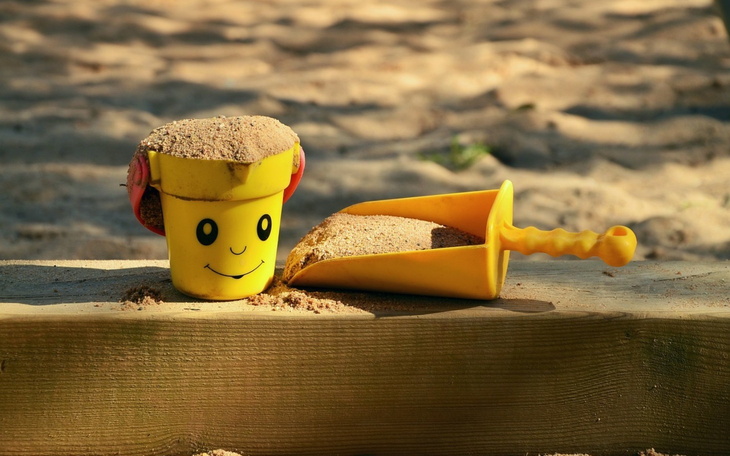 Zabawki do piasku: żółty kubełek i łopatka na plaży.