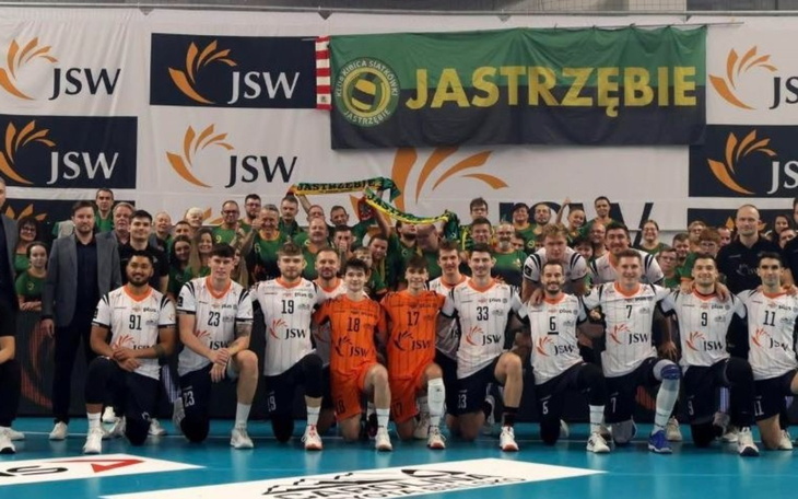 Zespół siatkarski pozujący na tle banera.