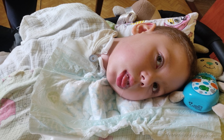 Chłopiec leżący na łóżku, z uśmiechem i zabawkami obok.