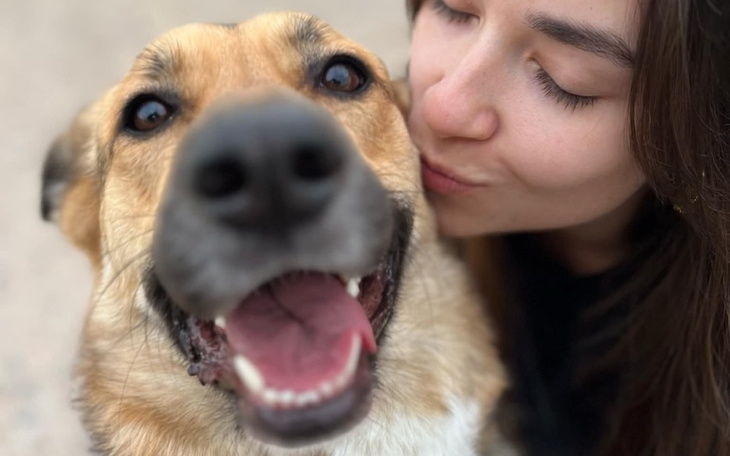 Kobieta całuje psa, oboje uśmiechnięci.