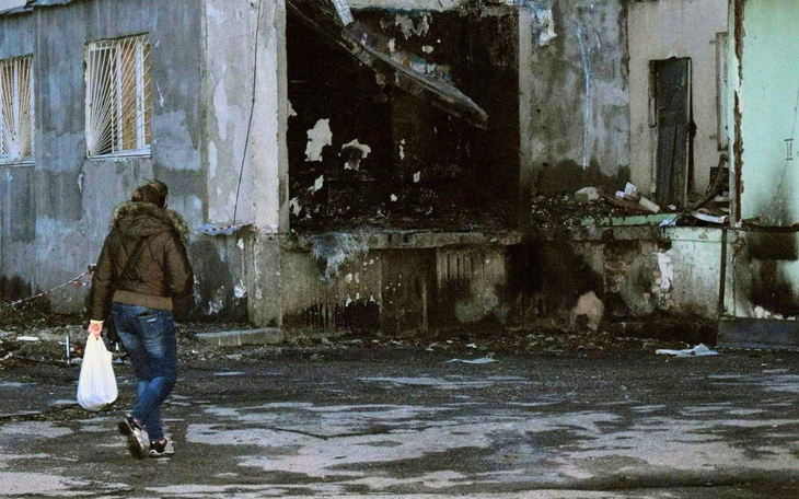 Kobieta z torbą przechodzi obok zniszczonego budynku.