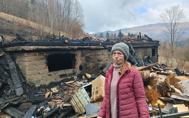 Kobieta stoi wśród zniszczeń po pożarze, w tle zrujnowany budynek.